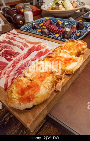 Dorfbrot Toast mit Olivenöl und zerkleinerten Tomaten, Scheiben von iberischem Schinken und Tintenfisch auf der Rückseite bedecken Stockfoto