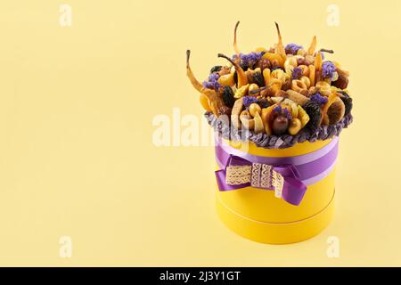 Gelbe zylindrische Box mit einem Flieder Bogen mit getrockneten Früchten auf einem gelben Hintergrund gefüllt, kopieren Raum Stockfoto