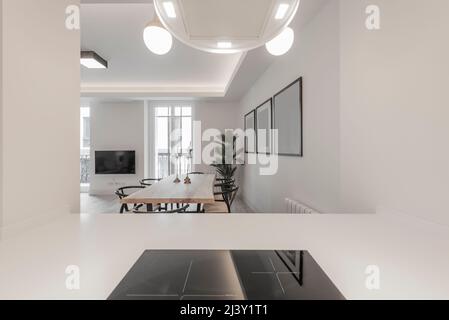 Designer-Küche mit weichen weißen Linien, integrierten Geräten und weiß lackierten Möbeln. Maiza Holz Esstisch und kombinierte Steinzeugböden, TV Stockfoto