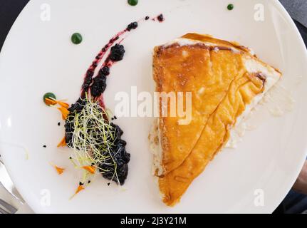 Käsekuchen in Nahaufnahme von oben mit Brombeermarmelade-Dekoration an der Seite auf weißem Teller schneiden Stockfoto