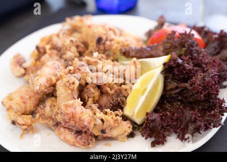 Baby-Tintenfische auf dem Teller mit Zitronenscheiben, Salat und Tomaten. Traditionelle spanische Tapas mit Meeresfrüchten Stockfoto