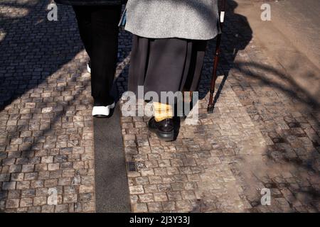 Ältere Frau mit einem Stock, die die Straße entlang geht, Rückansicht. Altes Paar, das die Hände zusammenhält, das Konzept des Alters, Erkrankungen der Gelenke und Stockfoto