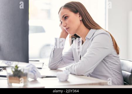 Dieser Job ist so langweilig. Aufnahme einer attraktiven jungen Geschäftsfrau, die allein im Büro sitzt und sich beim Umgang mit ihrem Computer gelangweilt fühlt. Stockfoto