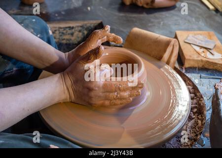 Hände eines Töpfers, wodurch ein irdenen Glas auf dem Kreis entsteht. Stockfoto