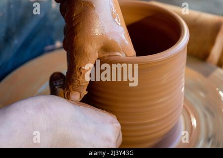 Hände eines Töpfers, wodurch ein irdenen Glas auf dem Kreis entsteht. Stockfoto
