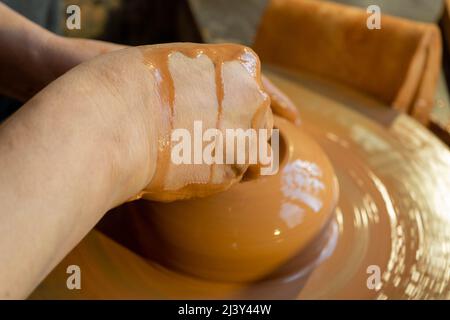 Nahaufnahme der Hände des Töpfers, die Tontopf auf dem Töpferrad in der Werkstatt Formen. Stockfoto