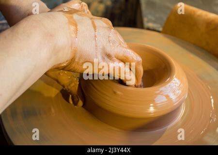 Nahaufnahme von männlichen Händen, die an einem Töpferrad arbeiten, um eine Schüssel zu machen. Stockfoto