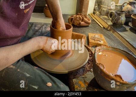 Ein Töpfermeister in einer alten Handwerkswerkstatt formt professionell mit seinen Händen einen Tontopf Stockfoto