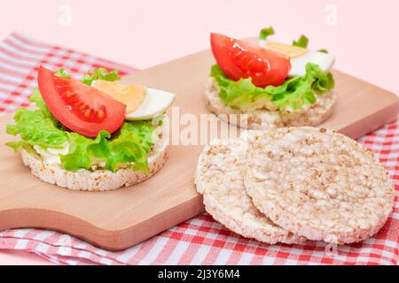 Reiskuchen-Sandwiches mit Tomaten, Salat und Ei auf Holzbrett. Einfaches Frühstück. Diät-Essen. Schnelle und gesunde Sandwiches. Knäckebrot mit leckerer Füllung. Gesunder Ernährungs-Snack Stockfoto
