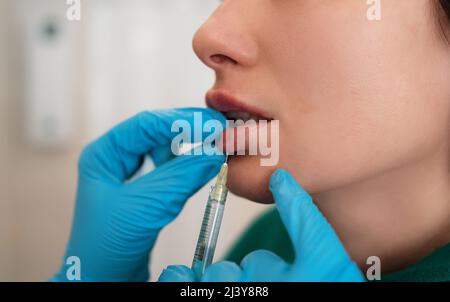 Junge Frau bekommt Hyaluronfüller oder Botox kosmetische Injektion in die Lippen, Nahaufnahme. Verjüngende Gesichtsbehandlung. Stockfoto