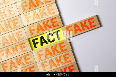 Geschäfts- und Designkonzept - surreale abstrakte geometrische Holzwürfel nehmen von Hand mit Wort TATSACHE und GEFÄLSCHTE Konzept auf Holzboden und weißem Hintergrund. Stockfoto