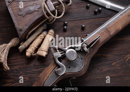 Uralte Steinschleudermuskete aus dem 17. Jahrhundert mit Pulverflasche und geführten Kugeln auf Holzdeck. Stockfoto