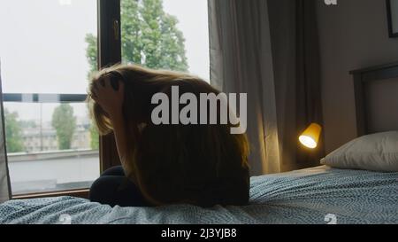Verwüstete kaukasische Frau, die ihr langes Haar berührte, zu Hause auf dem Bett saß und über Probleme nachdachte. Hochwertige Fotos Stockfoto