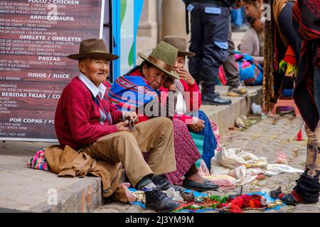 Peruanische Menschen, Männer und Frauen, sitzen auf dem Bürgersteig auf dem Pisac-Sonntagsmarkt, im Heiligen Tal, Peru. Stockfoto