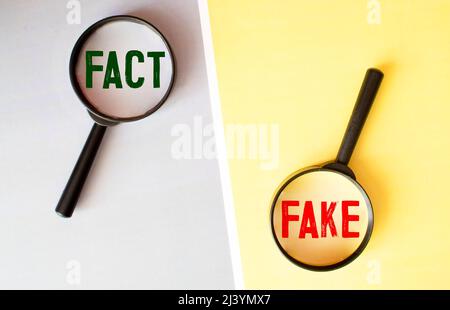 Eine Lupe, die auf die Worte Fake mit Buchstaben Spielblöcke auf einem hellen gelben Hintergrund gemacht. Konzeptuelles Bild von Unterscheidungsfakten fr Stockfoto