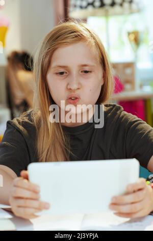 Modernes Kind in grauem Hemd mit Tablet-PC Fernunterricht zu Hause an sonnigen Tagen. Stockfoto