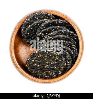 Senbei, japanische Sesamcracker, in einer Holzschale. Knusprige makrobiotische Cracker aus braunem Reis, schwarzen Sesamsamen und Sojasauce. Knackiger Snack. Stockfoto