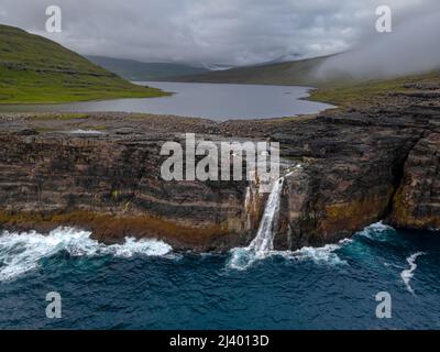 Wunderschöne filmische Luftaufnahme des Wasserfalls von Bøsdalafossur und des Sees von Trælanípan - Lagune herrliche Wahrzeichen auf den Färöer Inseln Stockfoto