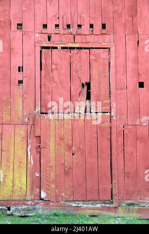 Verwitterte, rote Holztür einer alten Scheune. Stockfoto