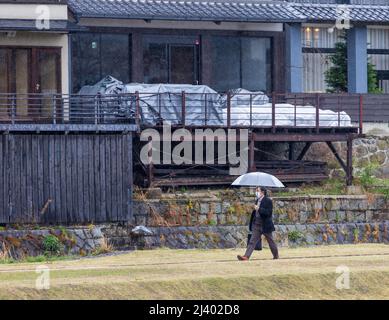 Einsame maskierte Geschäftsmann mit klaren Regenschirm Spaziergänge im Regen Stockfoto