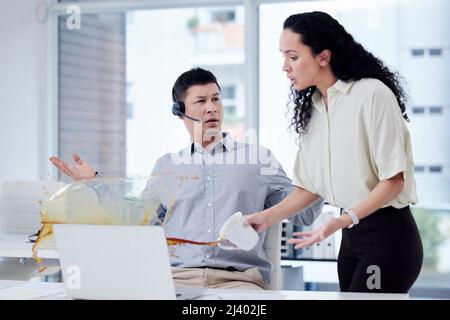 Wie ungeschickt kannst du sein. Aufnahme einer Geschäftsfrau, die eine Tasse Kaffee über den Schreibtisch eines Kollegen in einem Callcenter verschüttet hat. Stockfoto