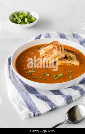 Eine Schüssel Tomatensuppe mit kleinen gegrillten Käse-Sandwich-Quadraten darauf. Stockfoto