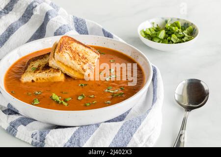 Eine Schüssel Tomatensuppe mit kleinen gegrillten Käsesandwiches darauf. Stockfoto