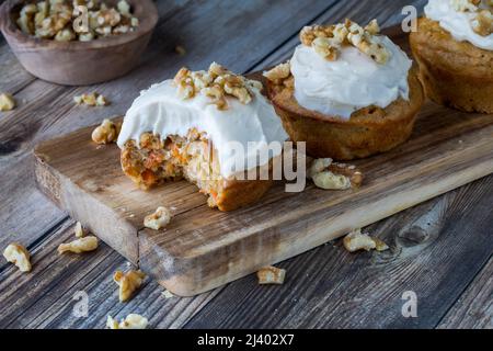 Karottenkuchenmuffins mit Frischkäse-Glasur und Walnüssen auf einem kleinen Holzbrett. Stockfoto