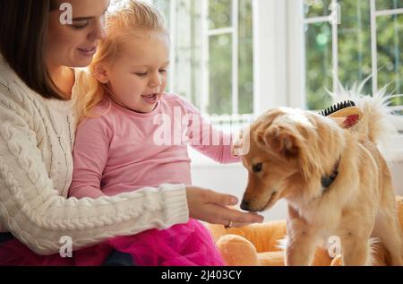 Es ist Ihr Tag der Verwöhnung. Aufnahme eines kleinen Mädchens, das auf dem Schoß ihrer Mutter sitzt, während sie ihren Welpen putzt. Stockfoto
