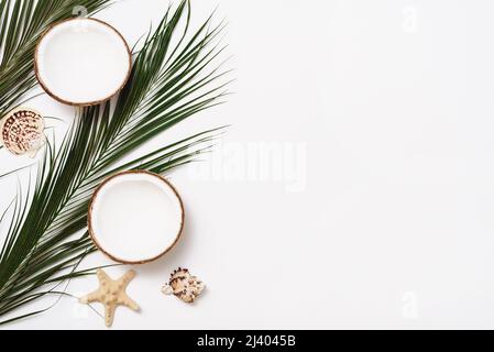 Palmblätter, Muscheln und Hälften einer Kokosnuss auf weißem Hintergrund. Flach liegend mit Kopierplatz. Sommerkomposition Stockfoto