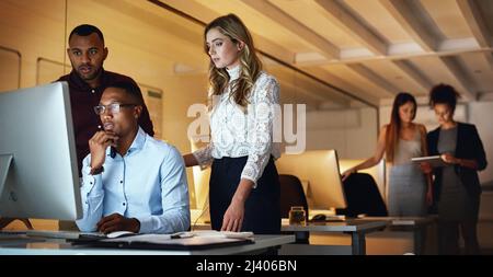 Konzentriert sich auf das Endergebnis. Aufnahme einer Gruppe von Geschäftsleuten, die nachts an einem Computer in einem Büro arbeiten. Stockfoto