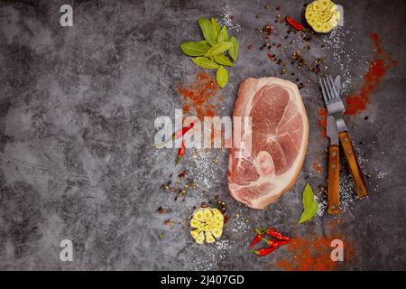 Rohe Schweinekoteletts mit Gewürzen auf dunklem Hintergrund. Draufsicht. Stockfoto