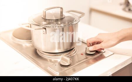 Weibliche Hand hält einen Topf, der in der Küche auf die elektrische Pfanne gelegt wird. Stockfoto