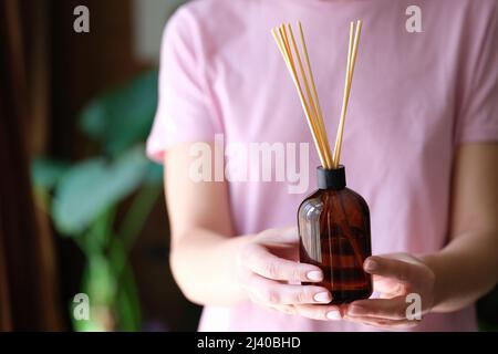Frau hält ein Glas mit Bambusstäbchen mit Lufterfrischer für die Nahaufnahme zu Hause Stockfoto
