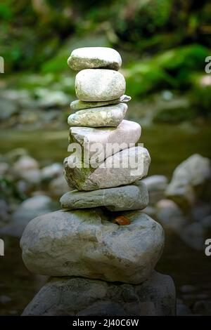 Haufen gestapelter Felsen, in hellem Sonnenlicht. Felsausgleich in einem Flussbett. Felsen, die flach auf einander zu großer Höhe gelegt wurden. Ausgeglichene Felsen. Stockfoto