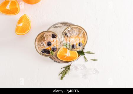 Draufsicht auf zwei Gläser mit Fruchtwasser aus Orange, Heidelbeeren, Eiswürfeln. Sommerliches kaltes Getränk. Durst in der Hitze löschen Stockfoto