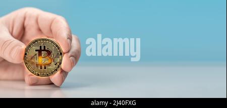 Mann Hand halten Bitcoin. Physische Bitmünze. Digitale Währung. Kryptowährung. Goldene Münze mit Bitcoin-Symbol auf hellblauem Hintergrund. Kopierraum Stockfoto