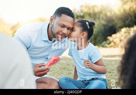 Nennen Sie es einen Stamm, nennen Sie es eine Familie. Aufnahme einer Tochter, die ihren Vater bei einem Picknick küsst. Stockfoto