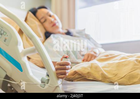 Patientin, die die Notruftaste gedrückt hat, während sie im Krankenhausbett liegt. Stockfoto