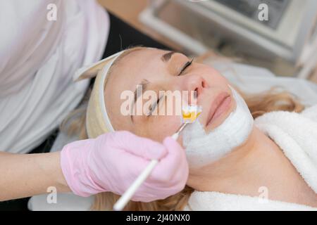 Gesichtspeeling-Maske, Beauty Spa, Hautpflege. Frau bekommt Gesichtsbehandlung durch Kosmetikerin im SPA Salon, Nahaufnahme Stockfoto