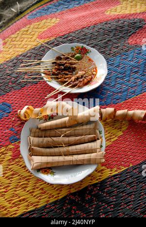 Schmackhafter Satay mit einer würzigen Sauce, gegessen mit Lontong, Reis in Palmblätter verpackt, am Senggigi Beach. Stockfoto