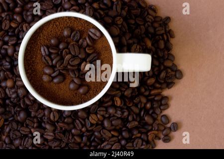 Frisch geröstete Kaffeebohnen im Hintergrund und gemahlener Kaffee in der Tasse oben. Hintergrund und Textur verfügbar. Kann für Cafés verwendet werden Stockfoto
