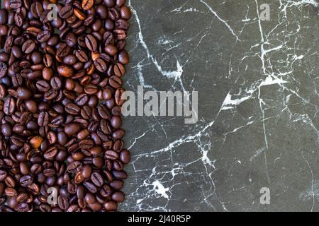 Frisch geröstete Kaffeebohnen von links auf grauem Hintergrund. Kann als Hintergrund- oder Textbereich verwendet werden. Stockfoto