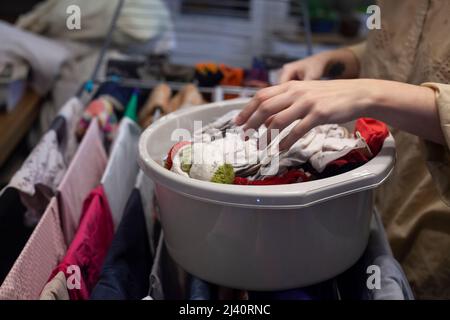 Eine Frau wäscht einem Kind zu Hause Dinge. Frauenunterricht über Mutterschaft. Trocknen nach dem Waschen. Das Mädchen enthüllt Kleidung. Ein Waschbecken mit Bettwäsche. Fa Stockfoto