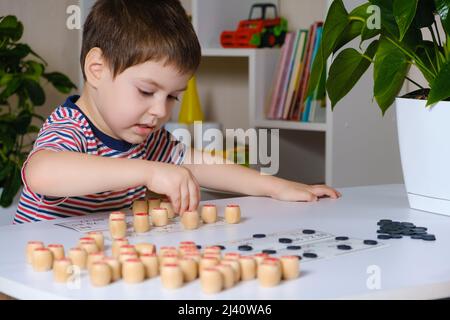 Ein 4-jähriger Junge spielt loto und studiert Zahlen anhand eines Brettspiels. Stockfoto