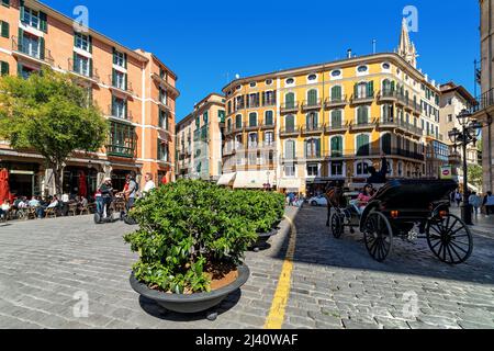 Menschen und Pferdekutsche auf einer gepflasterten Straße zwischen farbenfrohen Gebäuden im historischen Teil von Palma, Spanien. Stockfoto