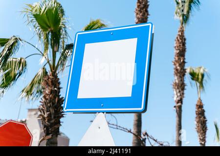 Leerer leerer Kopierraum blaues und weißes Straßenschild mit blauem Himmel und Palmen im Hintergrund. Mockup-Wegweiser Stockfoto