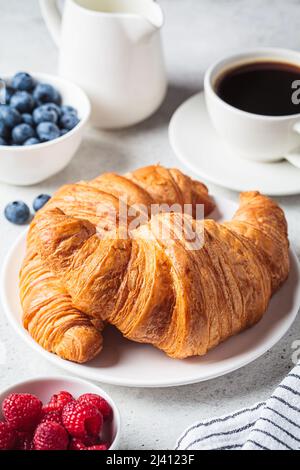 Leckeres Frühstück mit Croissants, Kaffee und Beeren, grauer Hintergrund. Stockfoto