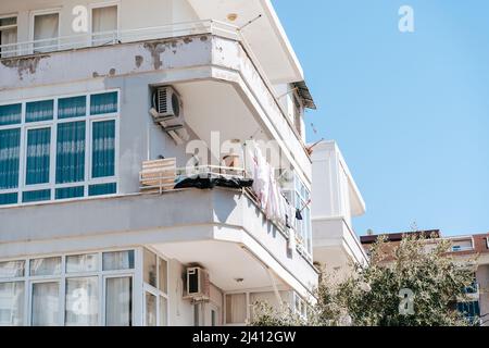 Weißes, heruntergekommenes, heruntergekommenes Wohnhaus mit Trocknungskleidung auf dem Balkon. Einfache Menschen leben. Abgewetzte, abgenutzte Wohnanlage mit alter Luft Stockfoto