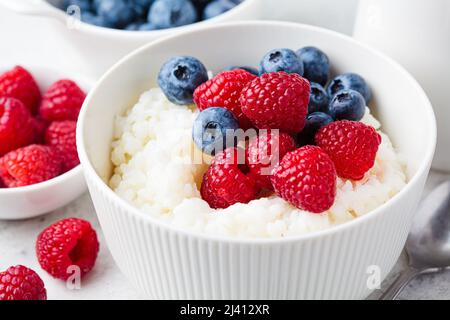 Reispudding mit Beeren und Butter, Nahaufnahme. Porridge Schüssel mit Himbeeren und Heidelbeeren. Gesundes Sommerfrühstück Rezept. Stockfoto